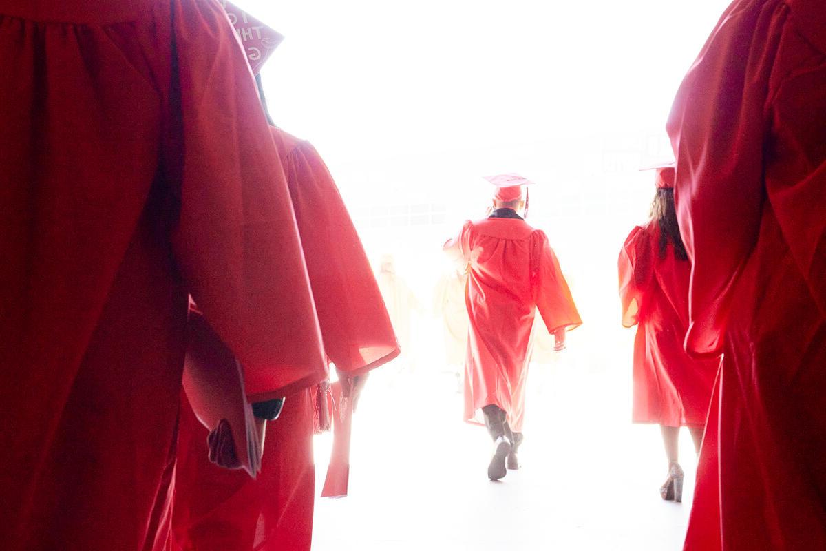 Students in cap and gown walking toward light